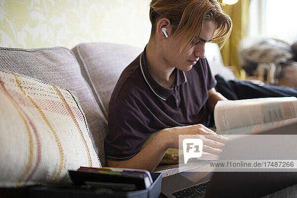 Jugendlicher mit Lehrbuch und Laptop beim Lernen zu Hause