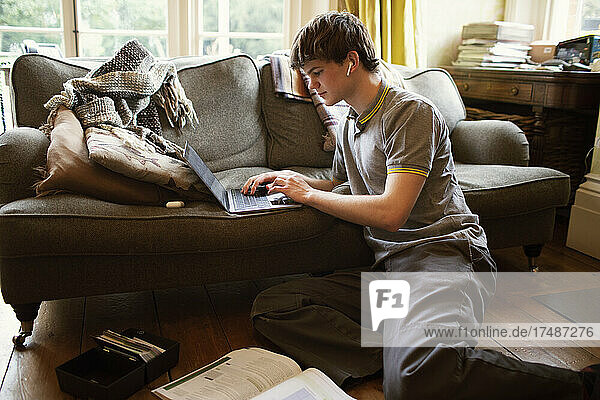 Focused teenage boy with laptop studying in living room at home