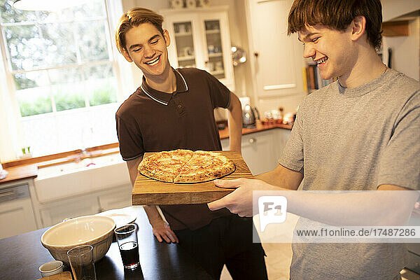 Happy teenage boys with pizza in kitchen