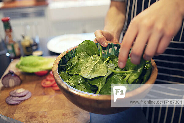 Close up teenage boy making spinach salad at home