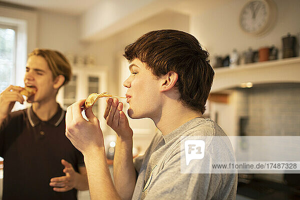 Teenage boys eating pizza in kitchen