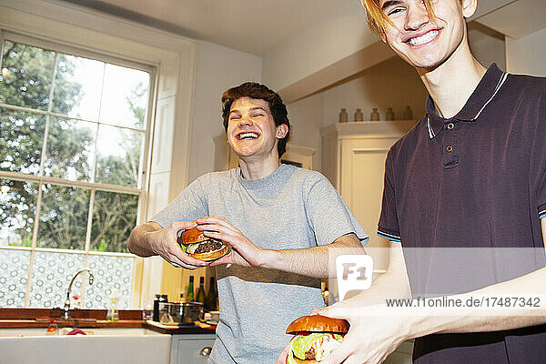 Porträt glücklicher Teenager-Jungs  die in der Küche Hamburger essen