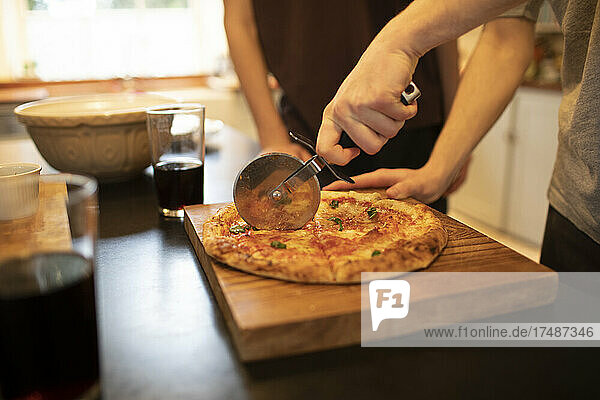 Boys slicing homemade pizza on cutting board in kitchen
