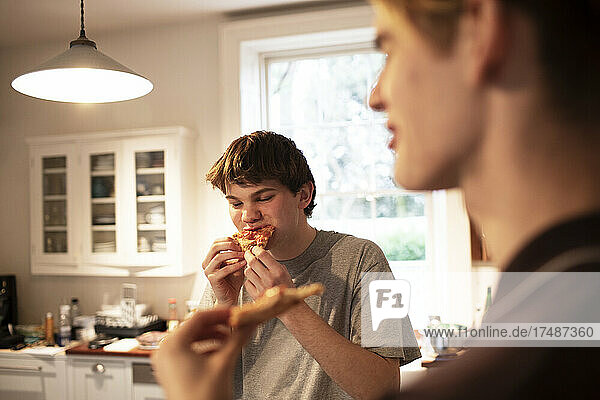 Teenage boys eating pizza in kitchen