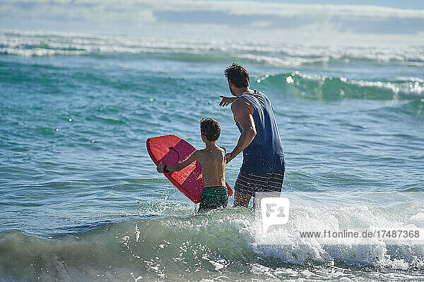 Father and son with body board watching ocean waves