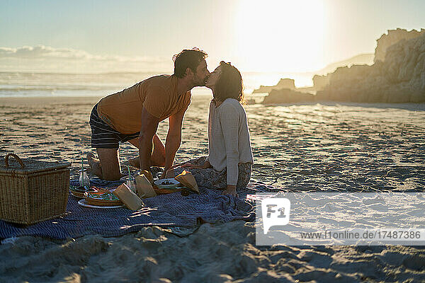 Zärtliches Paar  das sich auf einer Picknickdecke am sonnigen Sommerstrand küsst