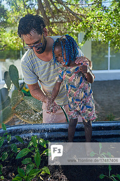 Vater und kleine Tochter gießen Pflanzen im Garten