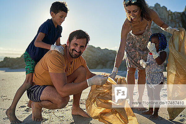 Portrait happy family picking up garbage on sunny beach