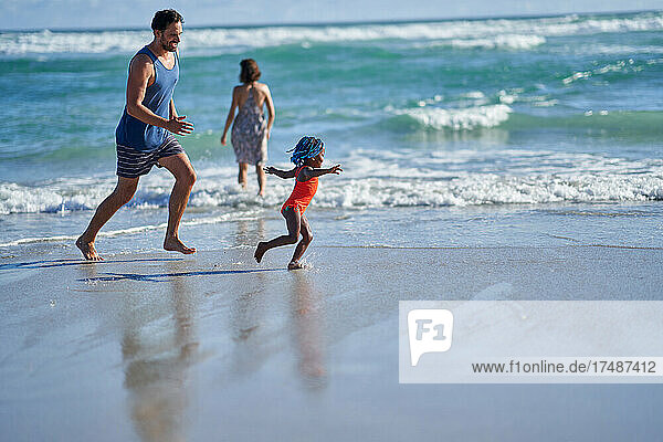 Glückliches Kleinkind Mädchen läuft auf sonnigen Ozean Strand mit Vater