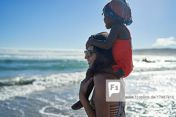 Mutter trägt süßes Kleinkind Tochter auf den Schultern auf Ozean Strand