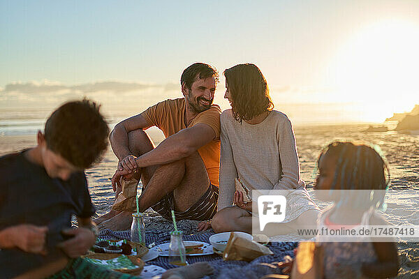 Glückliches Paar beim Picknick mit Kindern am sonnigen Sommerstrand
