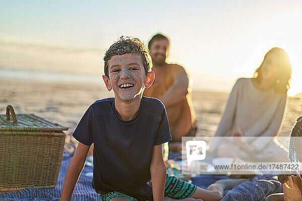 Portrait cute boy with sandy face on sunny beach with family