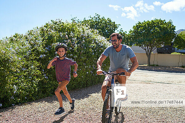 Happy father and son running and riding bike in sunny driveway