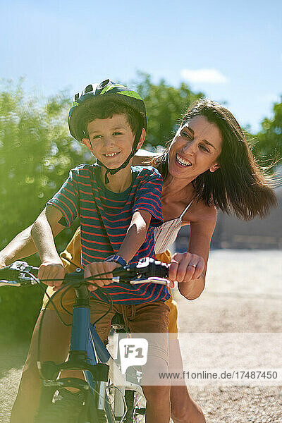 Glückliche Mutter mit Sohn beim Fahrradfahren in einer sonnigen Einfahrt