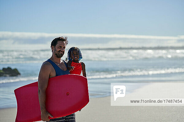 Glücklicher Vater und kleine Tochter mit Bodyboard am sonnigen Strand
