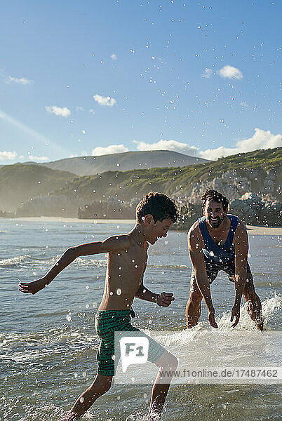 Happy playful father splashing son in sunny summer ocean