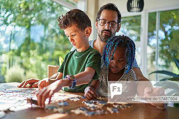 Vater und Kinder beim Zusammensetzen eines Puzzles zu Hause