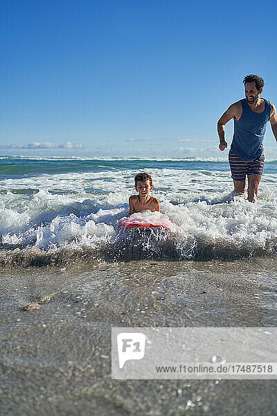 Vater und Sohn beim Bodyboarden in der sonnigen Meeresbrandung