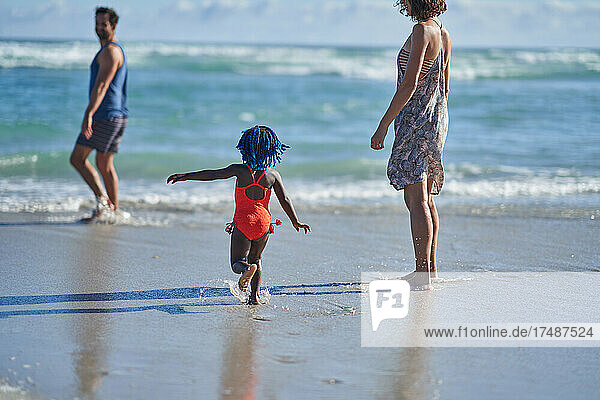 Nettes Kleinkind Mädchen spielen in sonnigen Ozean Brandung mit Eltern