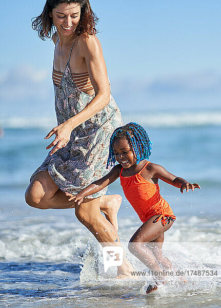Happy mother and toddler daughter running in sunny ocean surf
