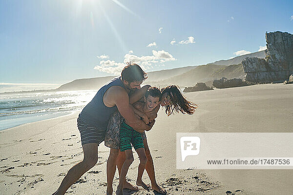 Happy playful family hugging on sunny summer beach