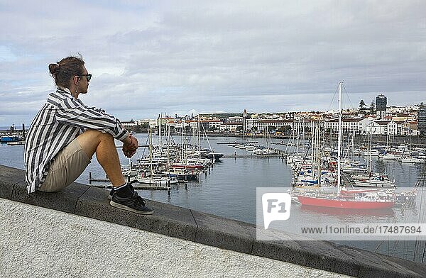 Junger Mann sitzt an der Promenade im Jachthafen von Ponta Delgada  Insel Sao Miguel  Azoren  Portugal  Europa