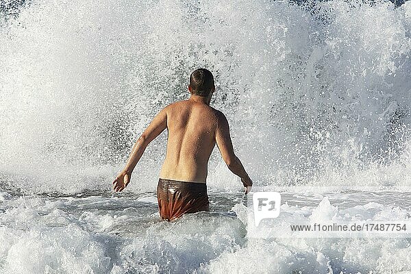 Junger Mann springt in eine hohe Welle am Strand von Praia de Santa Barbara  Ribeira Grande  Insel Sao Miguel  Azoren  Portugal  Europa
