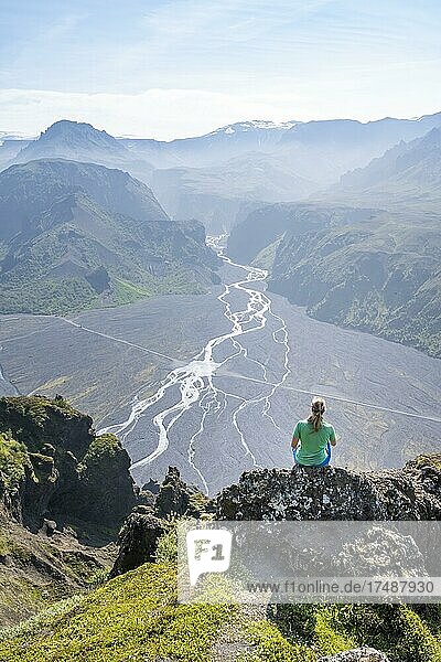Wanderin sitzt auf Felsen  Berge und Gletscherfluss in einem Bergtal  wilde Natur  hinten Gletscher Mýrdalsjökull  Isländisches Hochland  Þórsmörk  Suðurland  Island  Europa