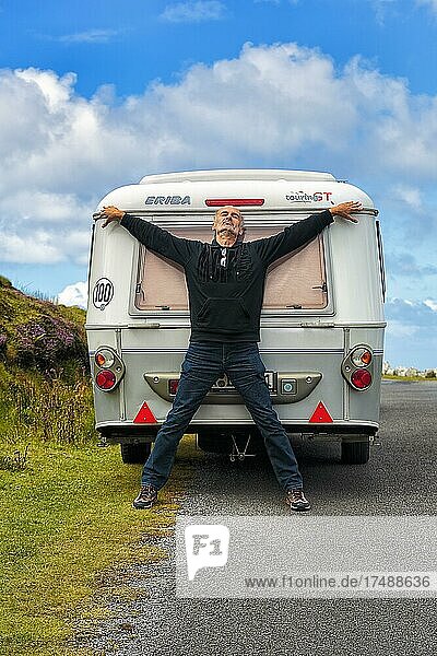 Mann lehnt an Wohnwagen am Straßenrand  macht Pause  Arme und Beine formen ein Kreuz  Panoramastraße Atlantic Drive  Achill Island  Mayo  Wild Atlantic Way  Irland  Europa
