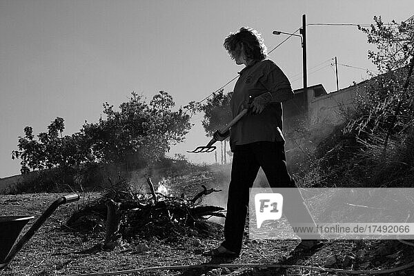 Frau mit Mistgabel vor Feuer mit Gartenabfällen  brennendes Holzfeuer mit Frau bei Gartenarbeit  Spanien  Europa