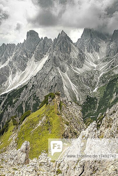 Wanderin steht auf einem Grat  hinten Berggipfel und spitze Felsen  dramatischer Wolkenhimmel  Cimon di Croda Liscia und Cadini-Gruppe  Auronzo di Cadore  Belluno  Italien  Europa