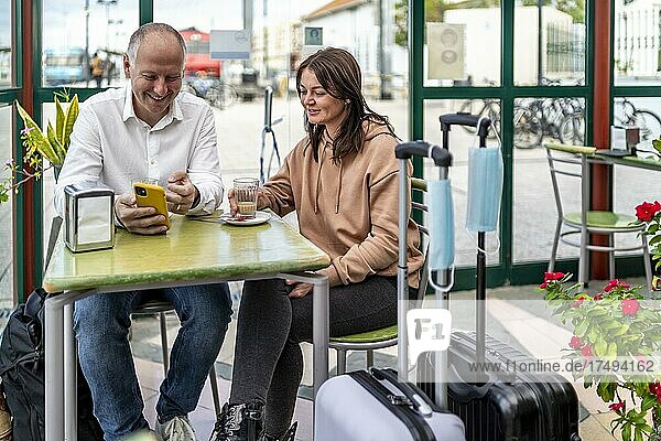A couple of travelers drinking coffee and checking something on the phone  The luggage with masks in the foreground  Portugal  Europe