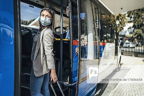 Junge Frau mit Gepäck und Schutzmaske beim Einsteigen in den Bus in Faro  Portugal  Europa