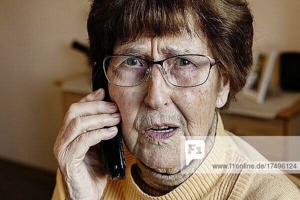 Senior citizen at home looking worried while phoning  grandson trick  Cologne  North Rhine-Westphalia  Germany  Europe