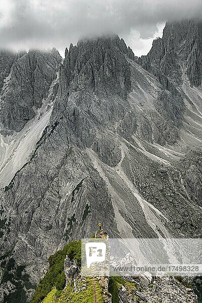 Wanderer steht auf einem Grat  hinten Berggipfel und spitze Felsen  dramatischer Wolkenhimmel  Cimon di Croda Liscia und Cadini-Gruppe  Auronzo di Cadore  Belluno  Italien  Europa