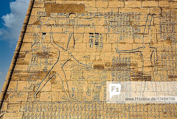 1. Pylon im Totentempel mit übergroßen Reliefdarstellungen geschmückt  die den Pharao in den typischen Machtdarstellungen beim Erschlagen der Feinde vor einer Gottheit zeigen  Medinet Habu  Totentempel Ramses III. Luxor  Theben-West  Ägypten  Luxor  Theben  West  Ägypten  Afrika