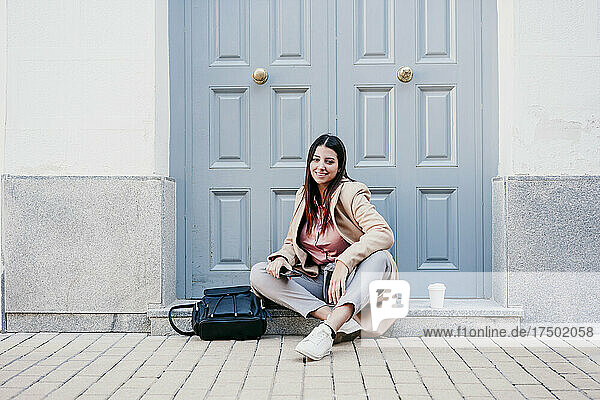 Smiling businesswoman sitting with backpack on doorstep