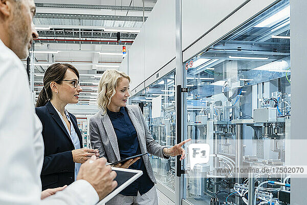 Businesswoman pointing at automated machinery discussing with coworkers in factory