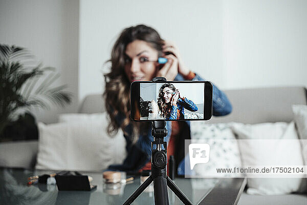 Vlogger applying mascara and influencing through smart phone at home studio