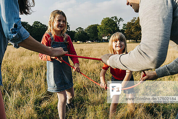 Daughters and parents holding hula hoop while playing in park