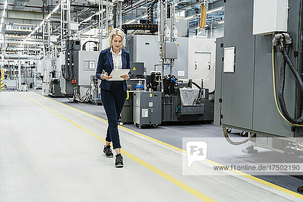 Businesswoman using tablet PC walking at modern factory