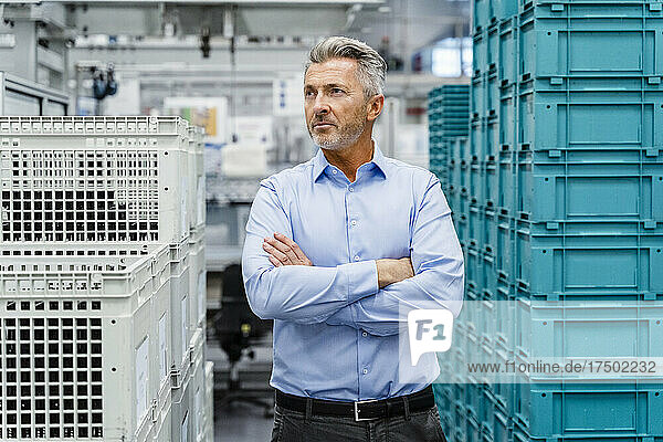 Thoughtful businessman with arms crossed amidst crates