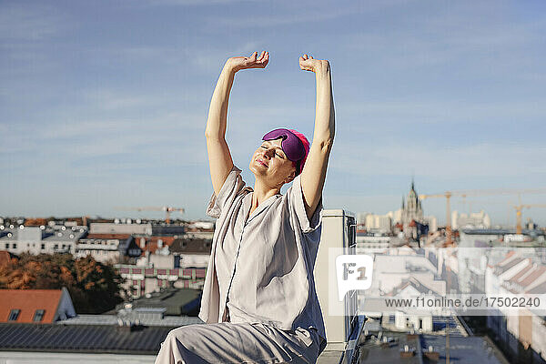Woman with hands raised sitting on rooftop