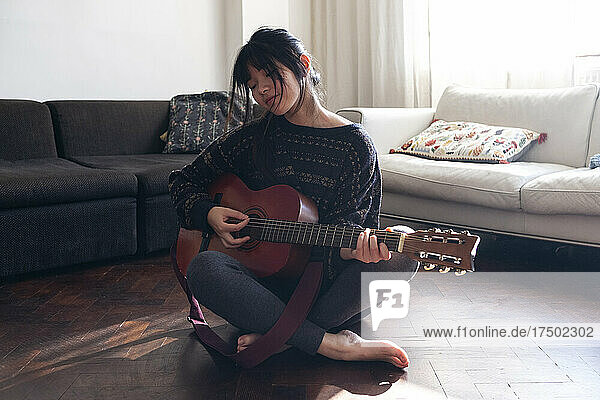 Woman playing guitar on floor in living room