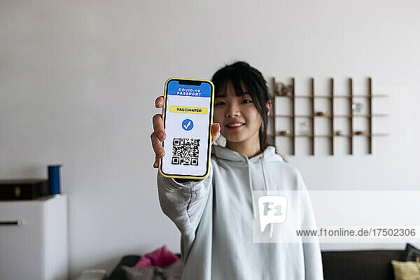 Young woman holding mobile phone with vaccination QR code on screen