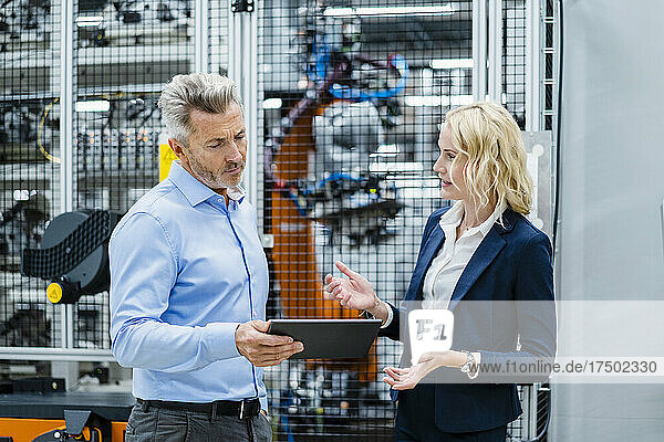 Businesswoman explaining businessman holding tablet PC at industry
