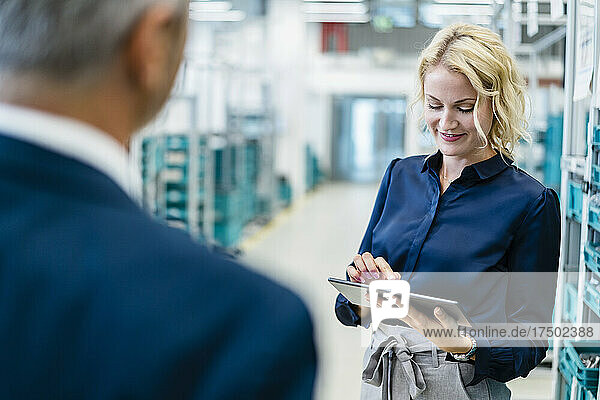 Smiling businesswoman using tablet PC with coworker in factory