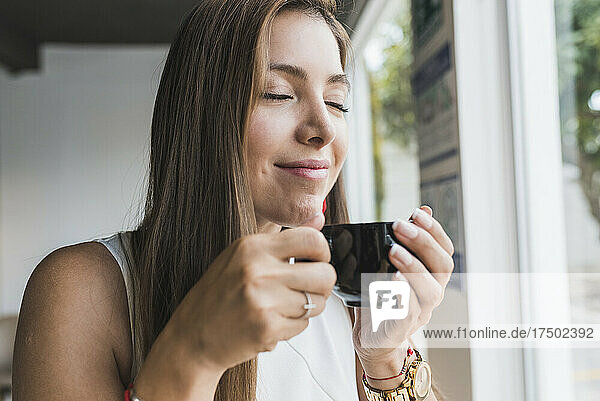 Frau mit geschlossenen Augen riecht Kaffee aus Tasse im Café