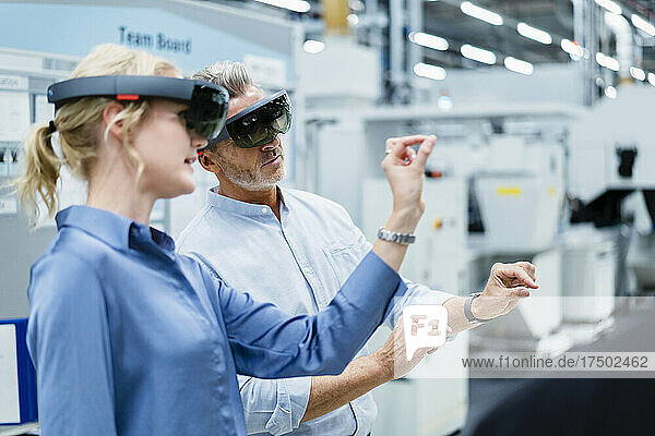 Coworkers discussing and using augmented reality eyeglasses in factory