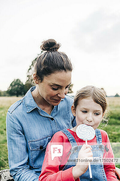 Mother looking at daughter eating lollipop in park